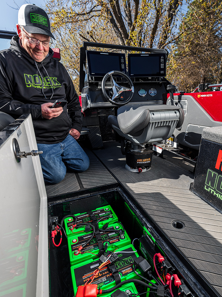 Angler using Norsk Guardian App next to 12V 180Ah Norsk Lithium Starting Battery on boat deck